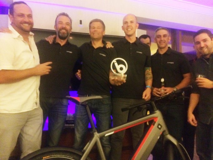 Team celebrating an industry award with a high-performance electric bike on display at an event.