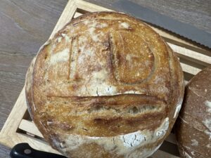Fresh sourdough bread with “ID” carved into the crust, on a wooden cutting board with a serrated bread knife.