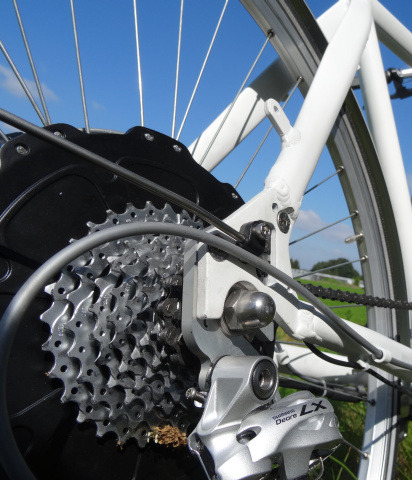 Close-up of an electric bike showcasing the TMM4 torque sensor in the rear dropout, with a sunny field background.